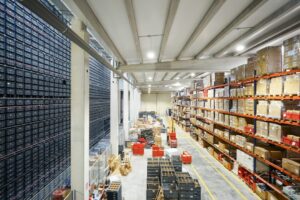 Hochregallager mit Kartons, Kunststoffboxen und markierten Transportwegen